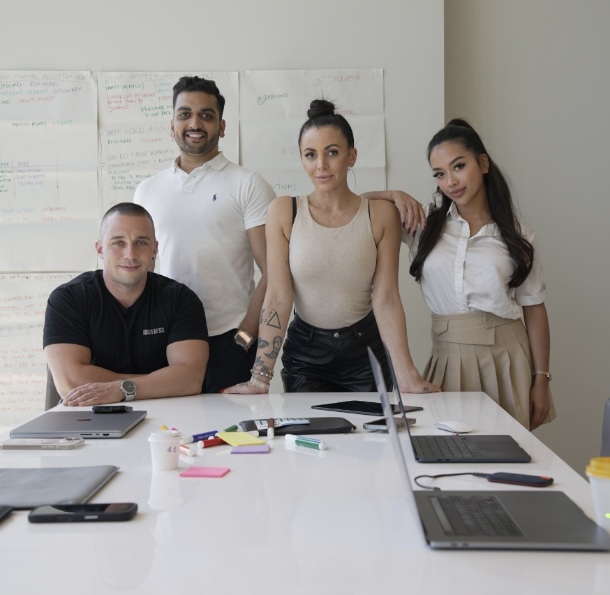 Four people working through a personal branding session around a white table, handwritten brand notes on the wall behind them